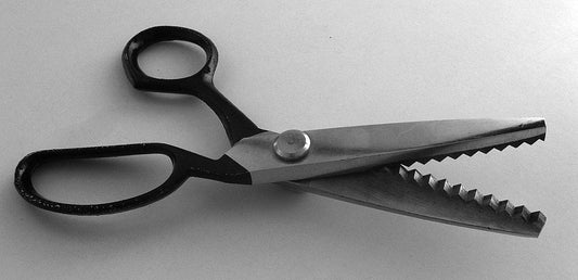 A pair opf silver and black pinking shears on a gray background